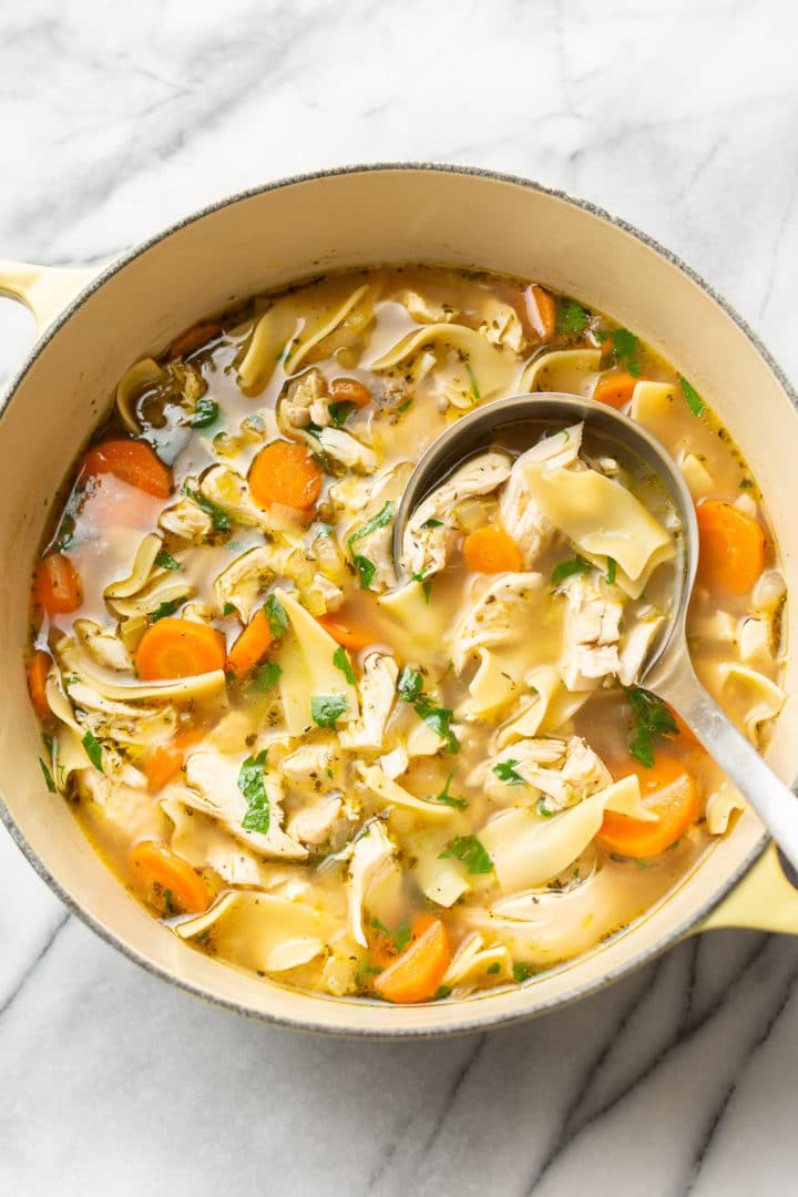 chicken noodle soup from scratch with egg noodles in a yellow pot with a ladle