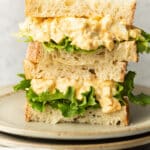 two egg salad sandwiches stacked on a plate