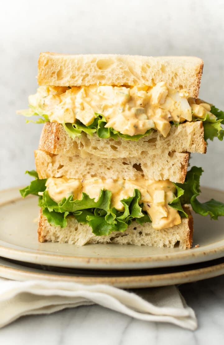 two egg salad sandwiches stacked on a plate