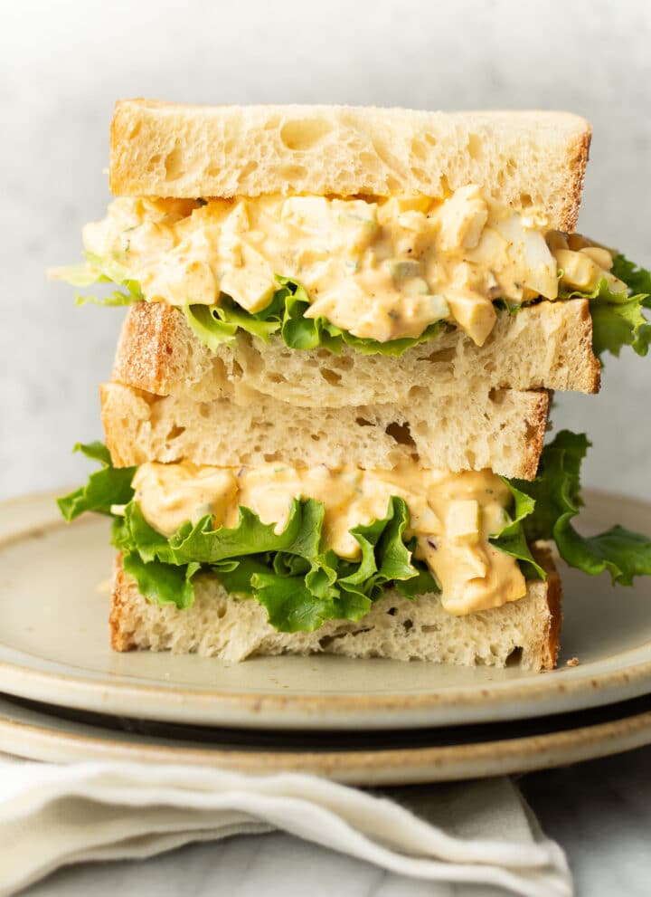 two egg salad sandwiches stacked on a plate