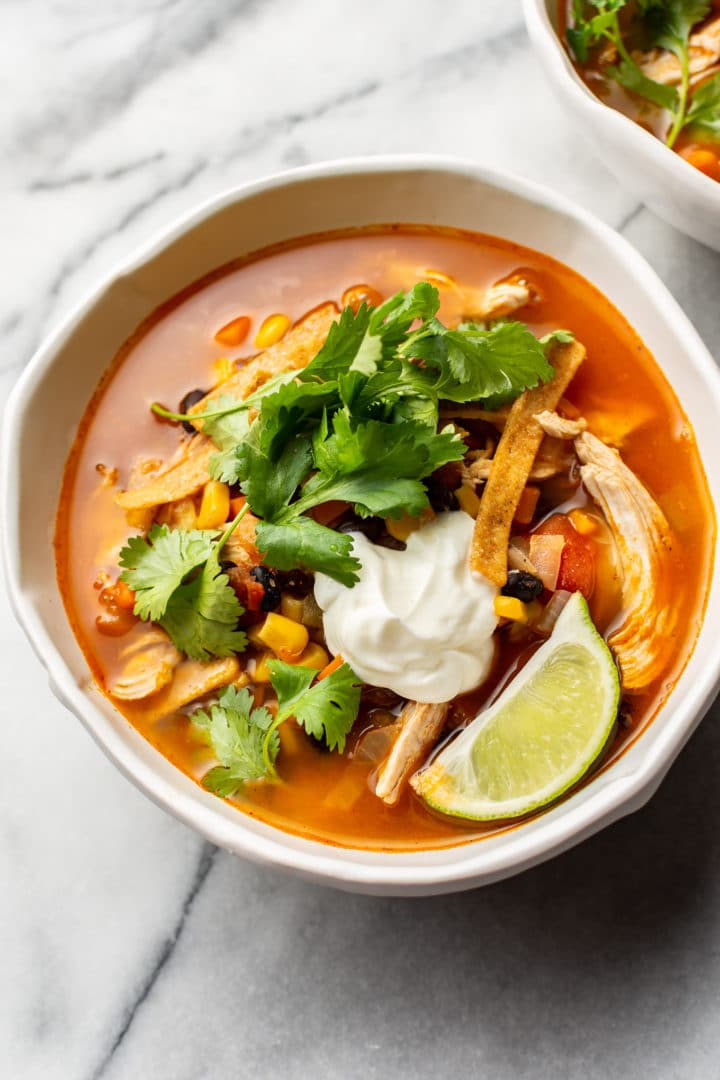 Mexican chicken tortilla soup in two white bowls on marble background