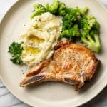 pan seared pork chops plated with buttery mashed potatoes and broccoli