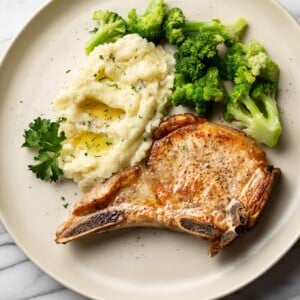 pan seared pork chops plated with buttery mashed potatoes and broccoli