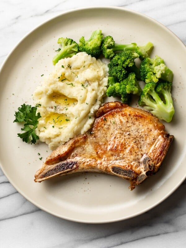 pan seared pork chops plated with buttery mashed potatoes and broccoli