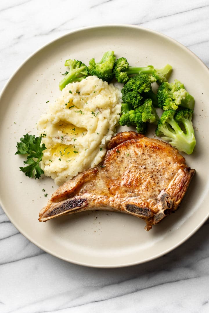 pan seared pork chops plated with buttery mashed potatoes and broccoli