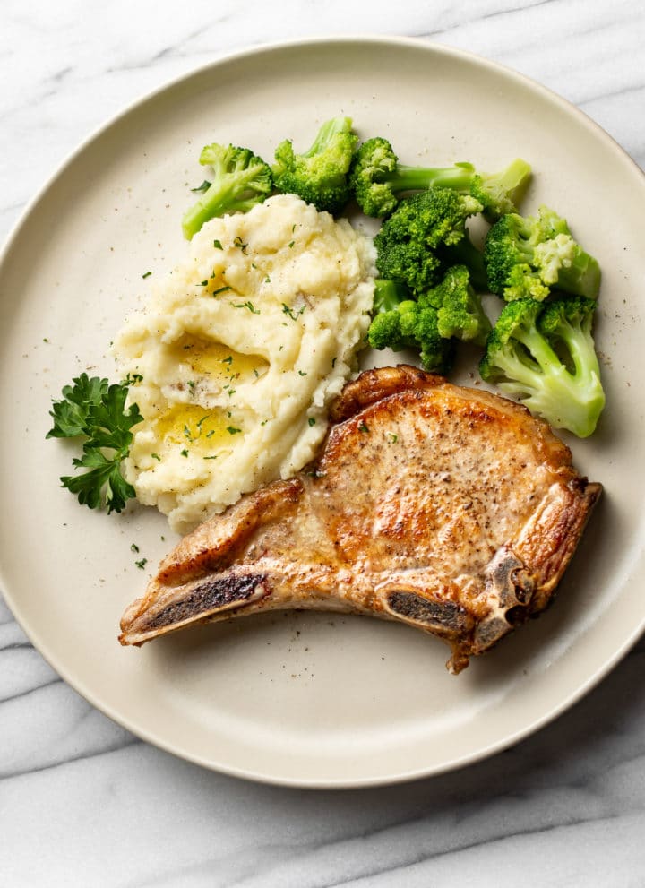 pan seared pork chops plated with buttery mashed potatoes and broccoli