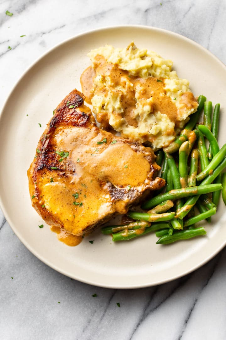 smothered pork chops on a plate with mashed potatoes, green beans, and gravy