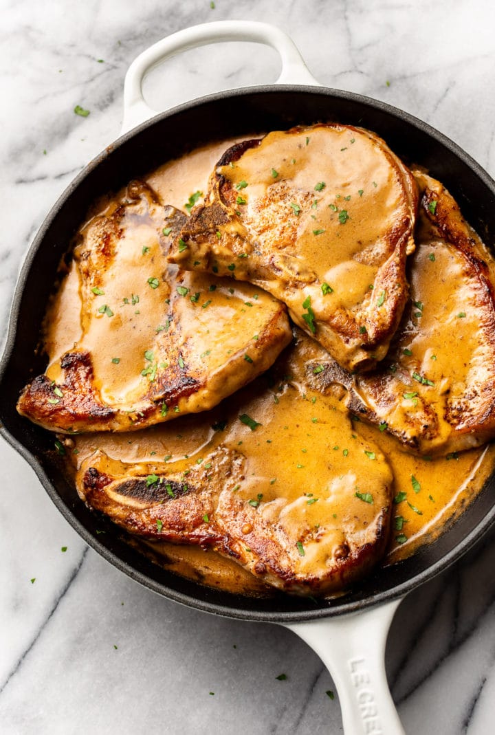 smothered pork chops in a skillet on a marble background