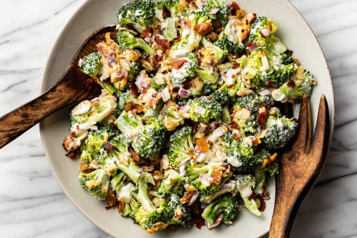 broccoli salad with wooden salad tongs in a shallow serving bowl