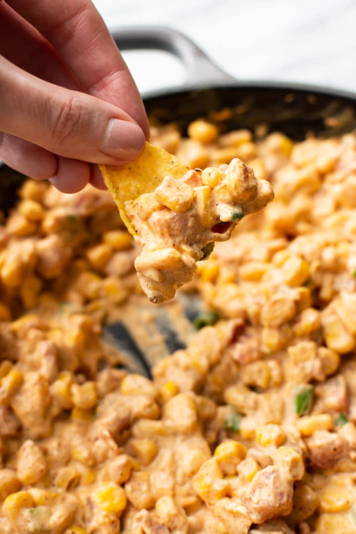 cream cheese corn dip in a skillet being scooped out with a tortilla chip