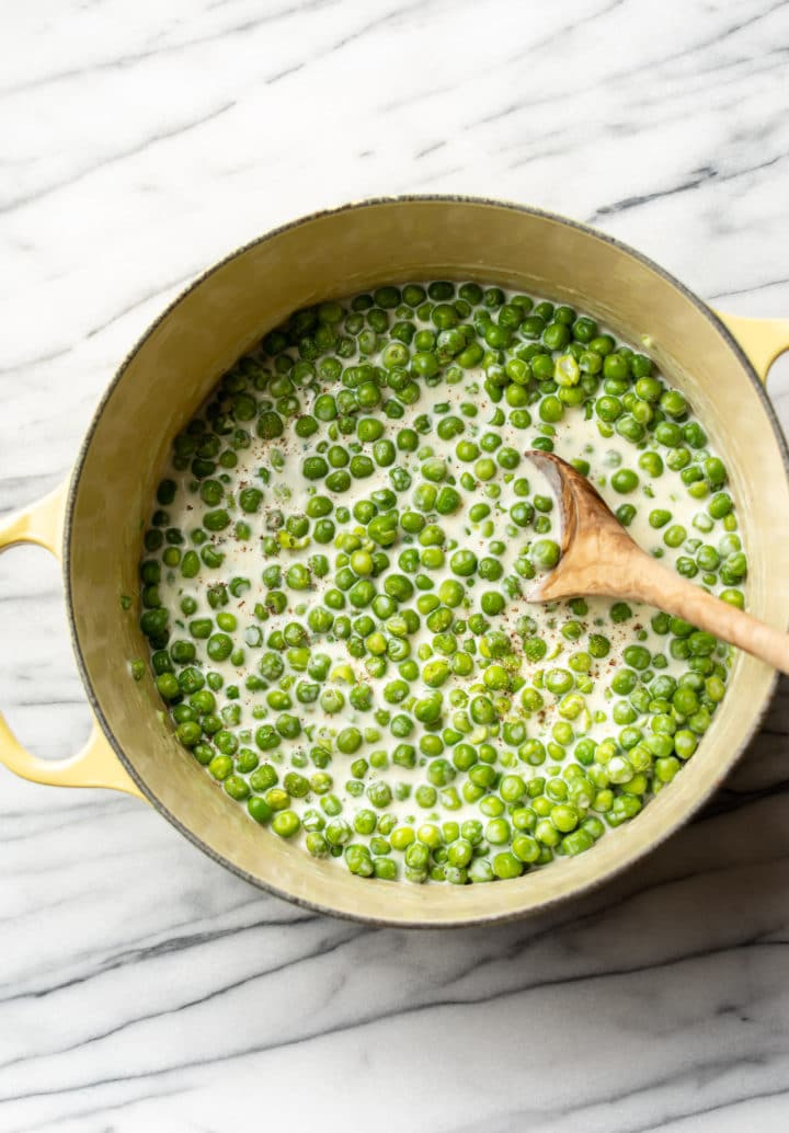 easy creamed peas in a yellow pot with a wooden spoon