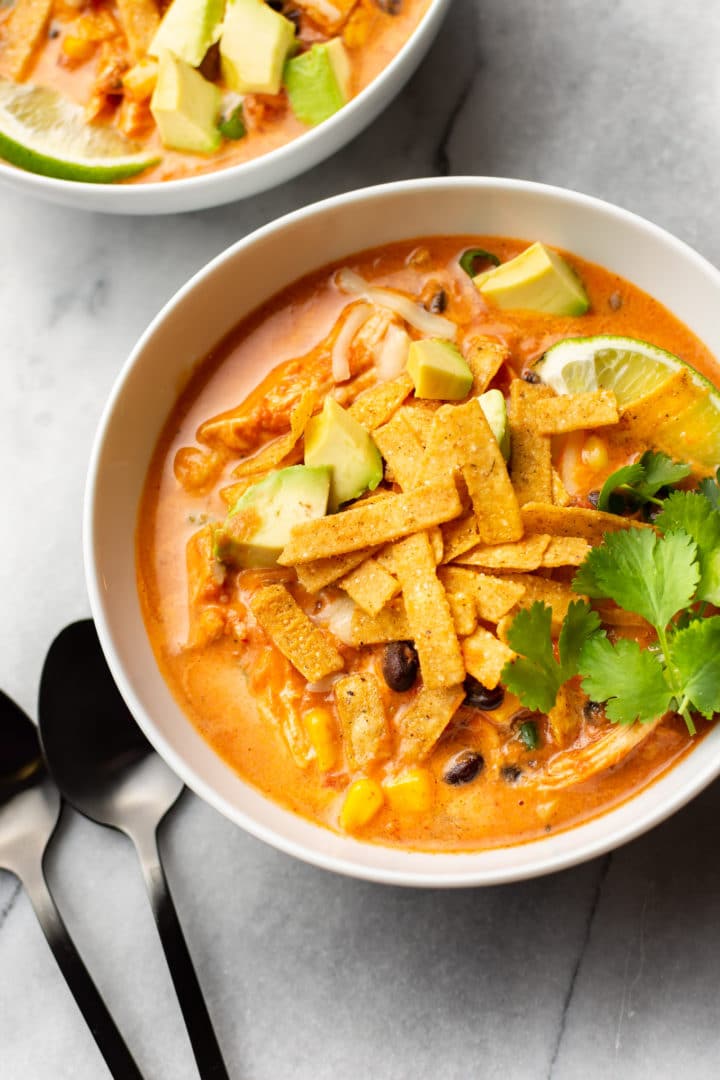 creamy Mexican chicken tortilla soup in two bowls with spoons on the marble background