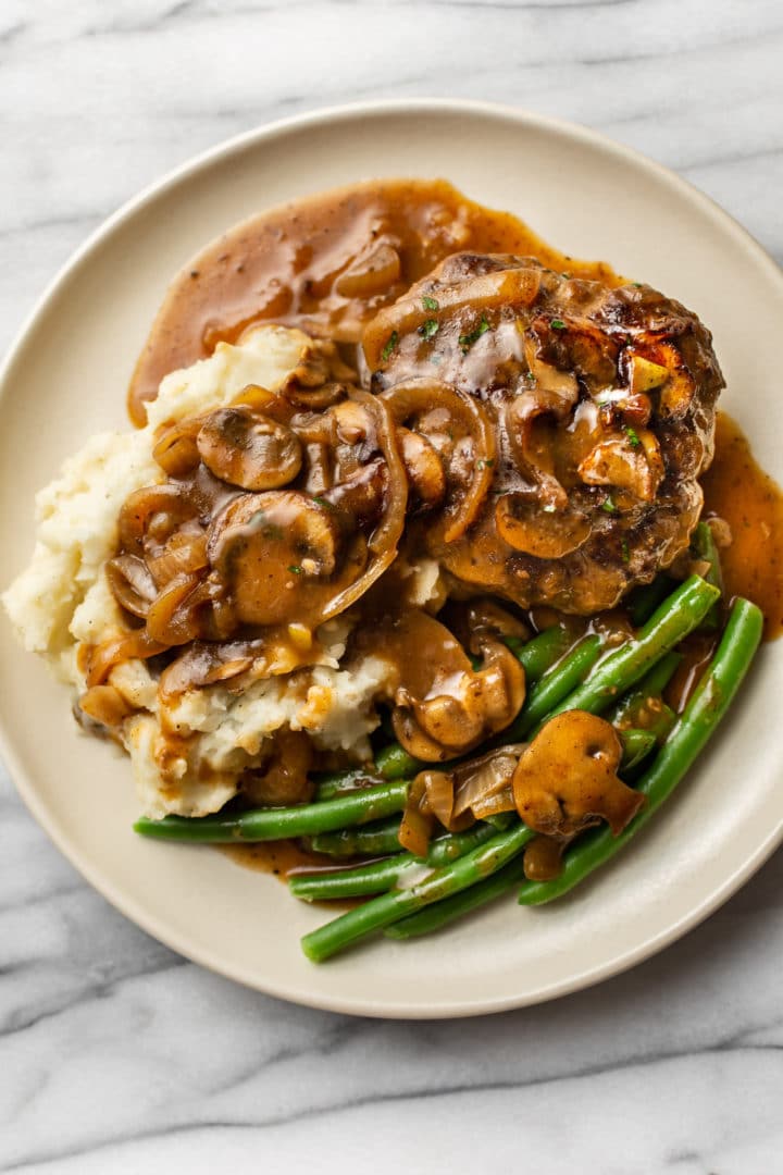 Salisbury Steak on a plate with mashed potatoes and green beans