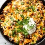 cheesy taco skillet topped with sour cream, scallions, and cilantro