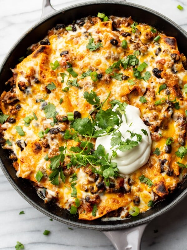 cheesy taco skillet topped with sour cream, scallions, and cilantro