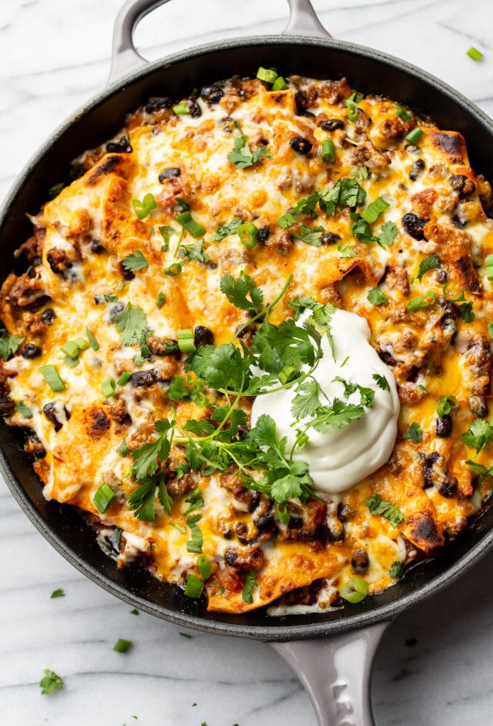 cheesy taco skillet topped with sour cream, scallions, and cilantro