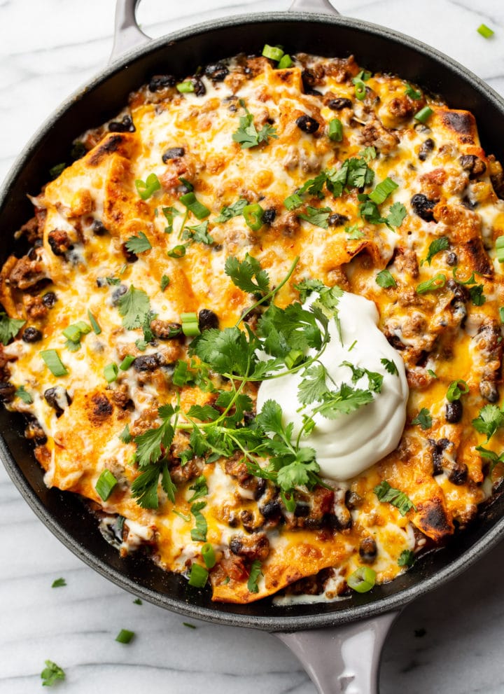 cheesy taco skillet topped with sour cream, scallions, and cilantro