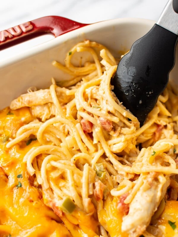 close-up of easy chicken spaghetti being lifted by tongs in a casserole dish