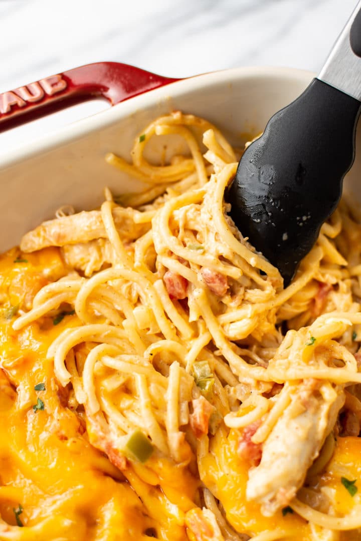 close-up of easy chicken spaghetti being lifted by tongs in a casserole dish