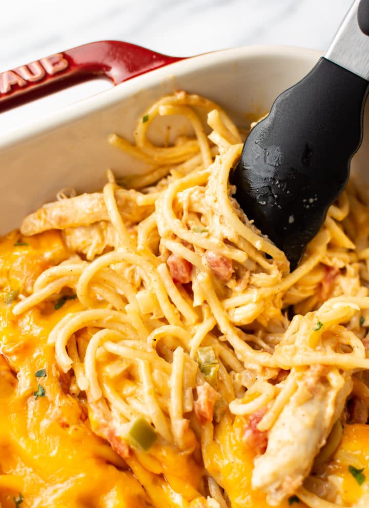 close-up of easy chicken spaghetti being lifted by tongs in a casserole dish