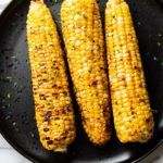 3 cobs of grilled corn on a black plate