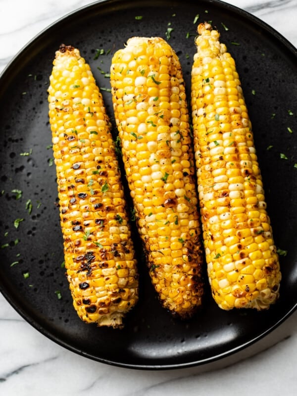 3 cobs of grilled corn on a black plate