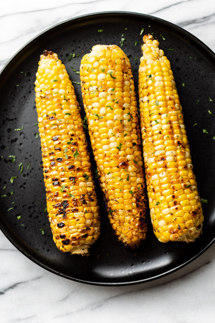 3 cobs of grilled corn on a black plate