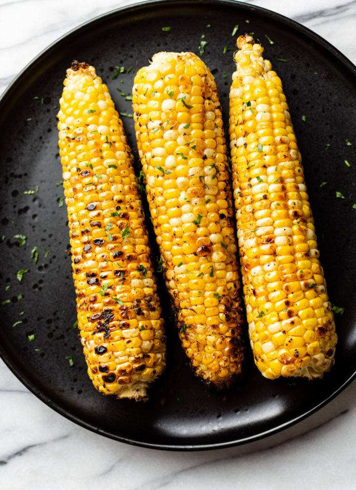 3 cobs of grilled corn on a black plate