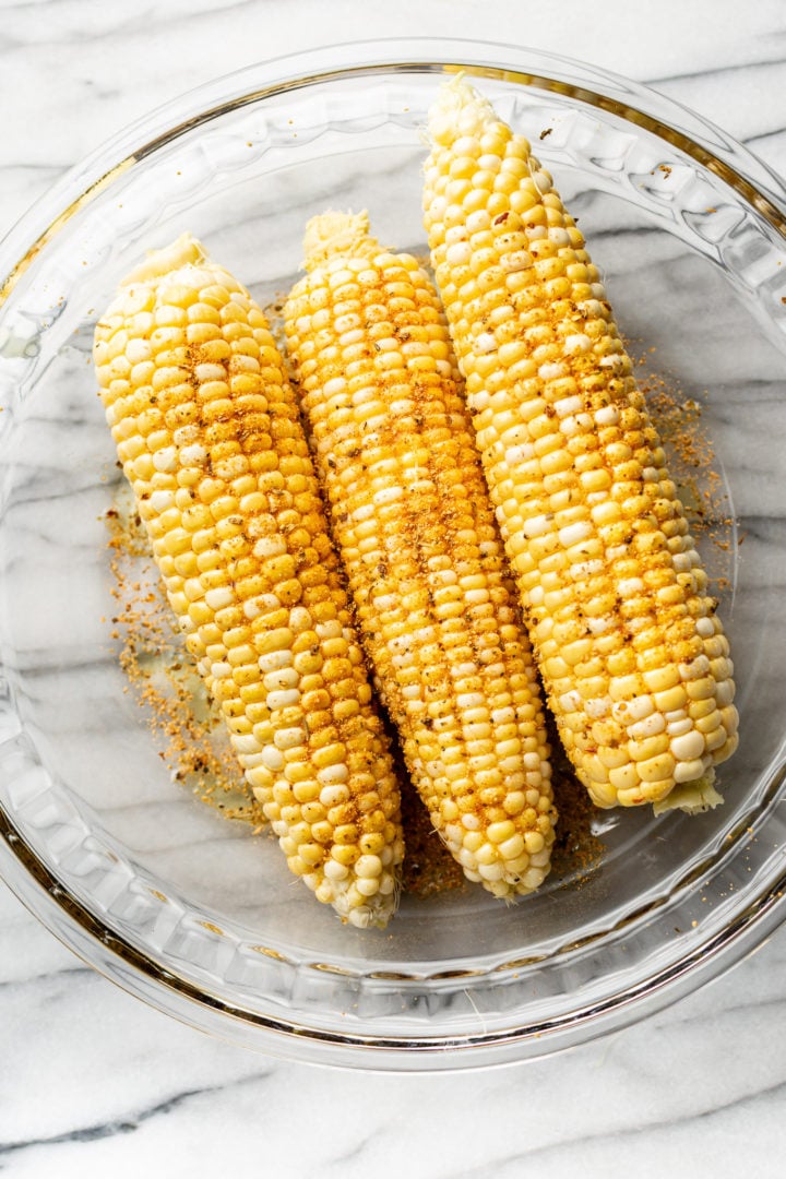 corn cobs coated with olive oil and Cajun seasoning in a glass prep bowl