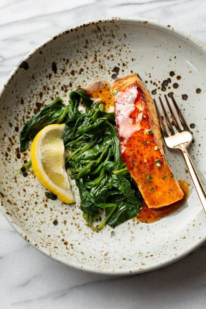 the best brown sugar salmon in a shallow bowl with spinach and a wedge of lemon