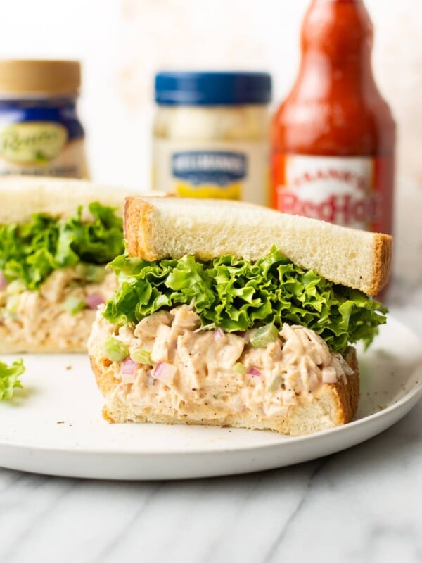 buffalo chicken sandwich cut in half surrounded by Frank's Red hot sauce, blue cheese dressing, and a jar of Hellmann's mayo