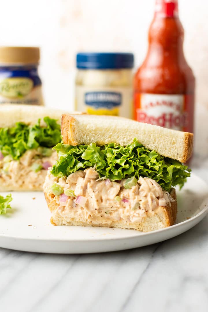 buffalo chicken sandwich cut in half surrounded by Frank's Red hot sauce, blue cheese dressing, and a jar of Hellmann's mayo