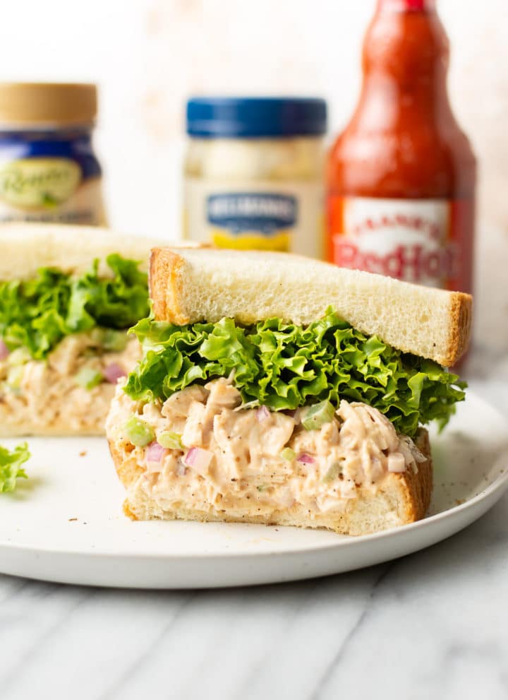 buffalo chicken sandwich cut in half surrounded by Frank's Red hot sauce, blue cheese dressing, and a jar of Hellmann's mayo