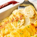 close-up of cheesy scalloped potatoes being lifted out of casserole dish with spatula