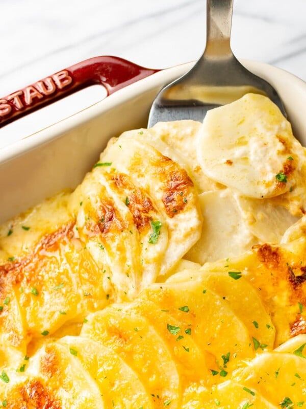close-up of cheesy scalloped potatoes being lifted out of casserole dish with spatula
