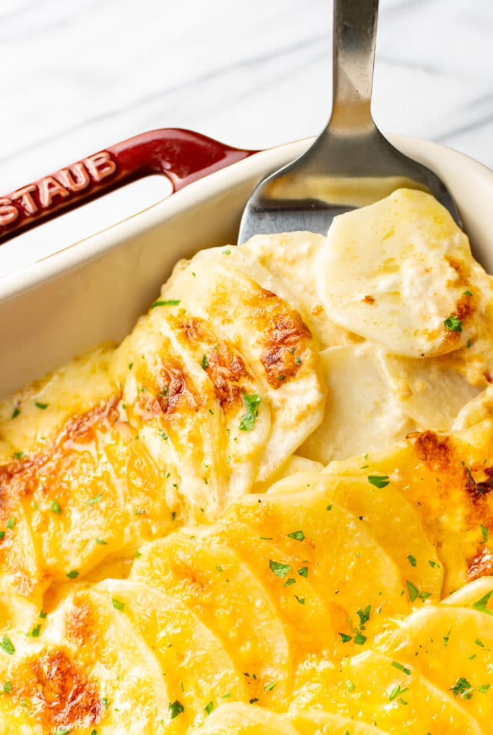 close-up of cheesy scalloped potatoes being lifted out of casserole dish with spatula