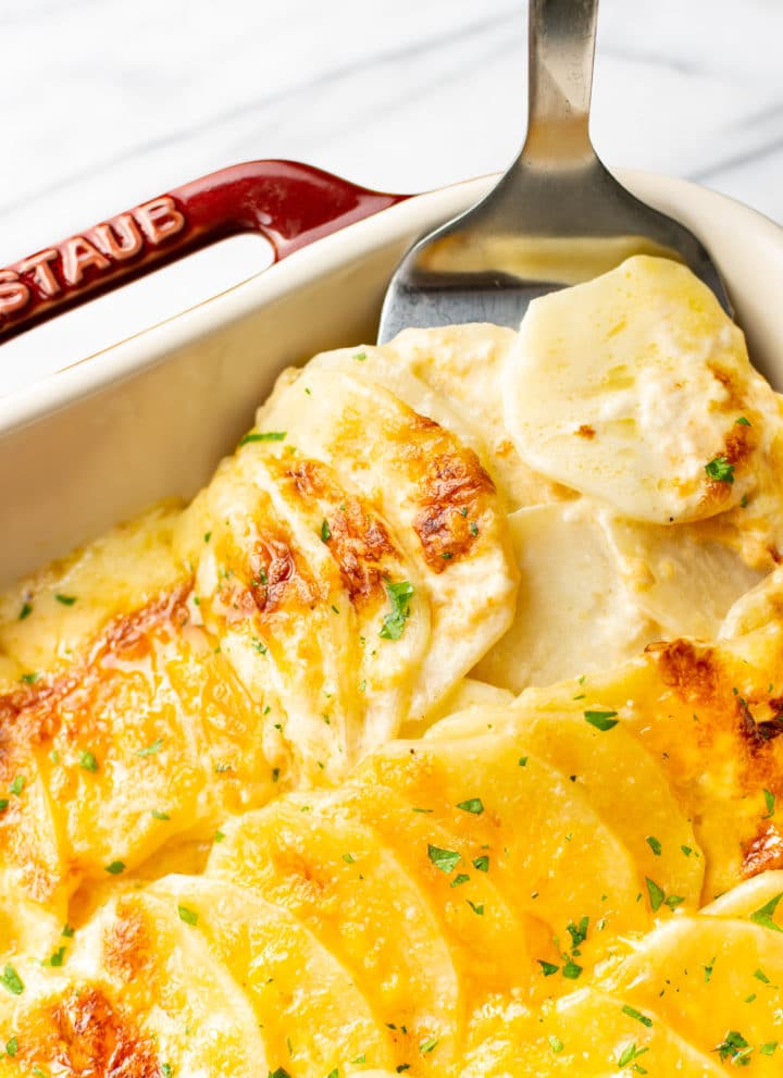 close-up of cheesy scalloped potatoes being lifted out of casserole dish with spatula