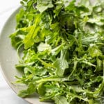 classic parmesan arugula salad being lifted out of a serving bowl with tongs