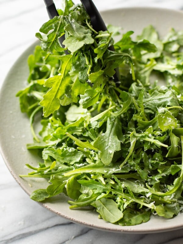 classic parmesan arugula salad being lifted out of a serving bowl with tongs