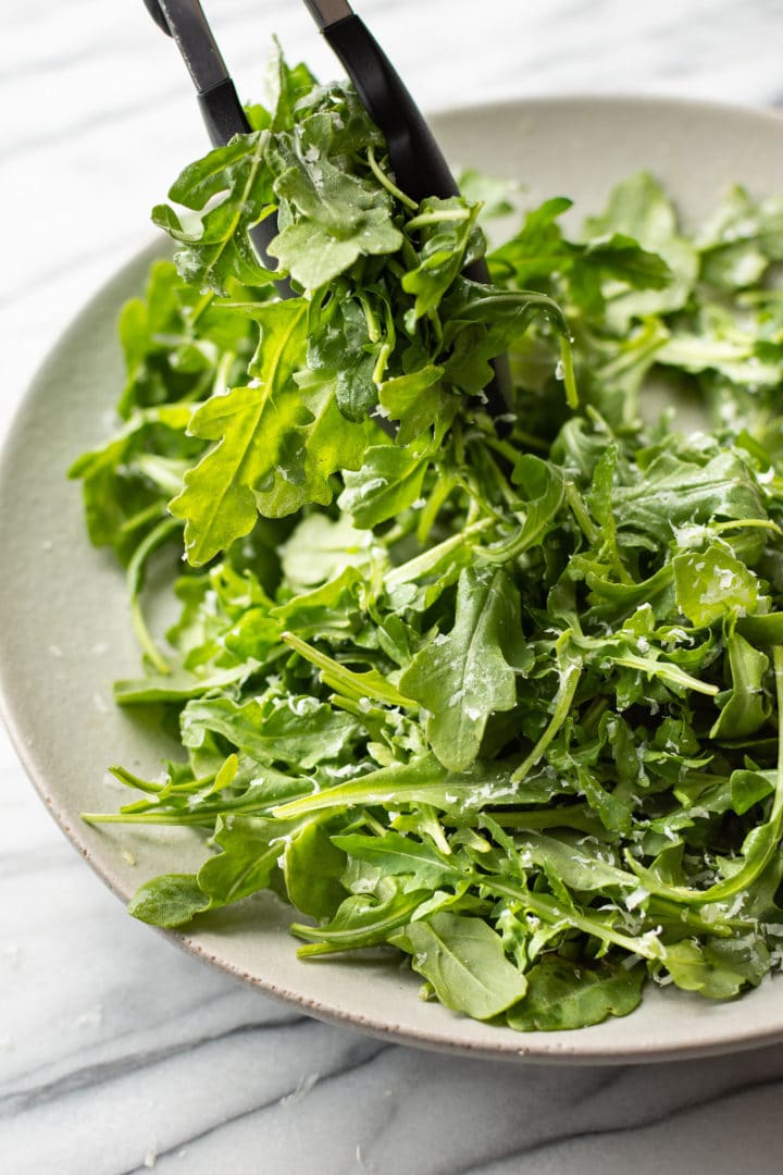 classic parmesan arugula salad being lifted out of a serving bowl with tongs