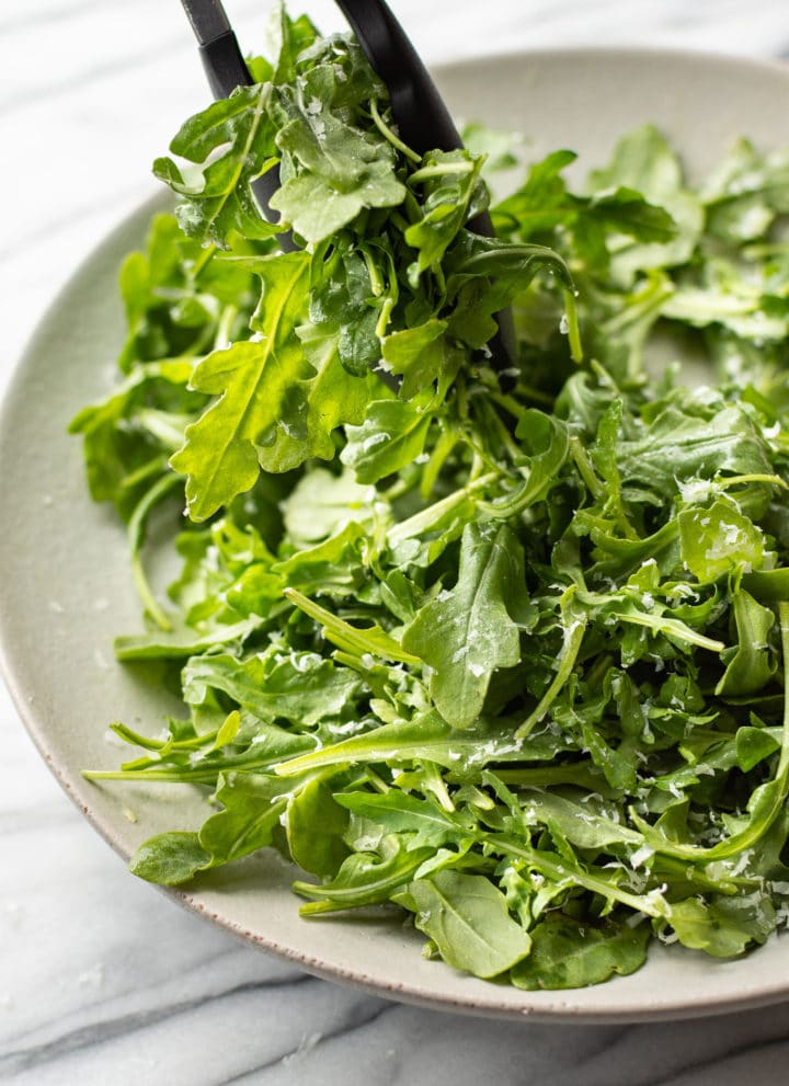 classic parmesan arugula salad being lifted out of a serving bowl with tongs