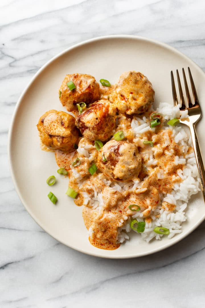 buffalo chicken meatballs on a plate with rice and scallions with a golden fork on the side