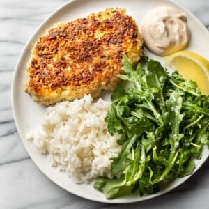 chicken patties on a plate with rice, remoulade sauce, arugula salad, and a lemon wedge