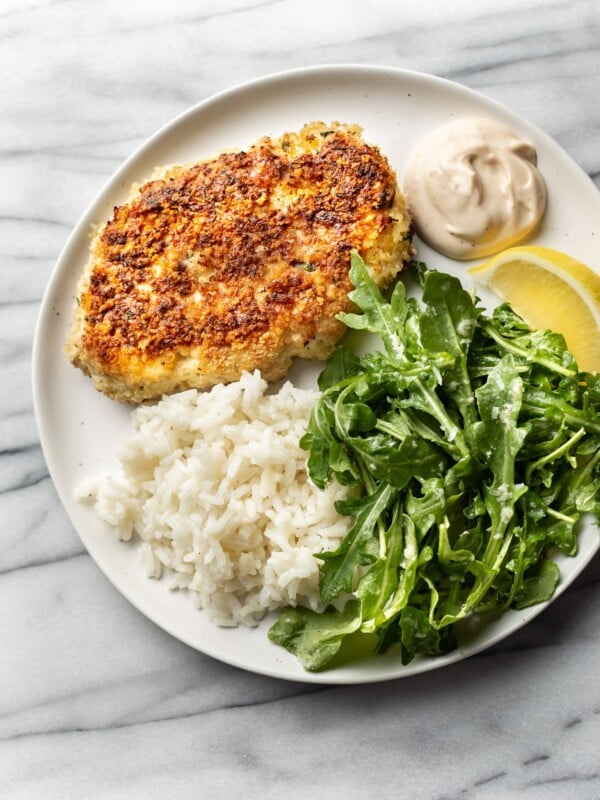 chicken patties on a plate with rice, remoulade sauce, arugula salad, and a lemon wedge
