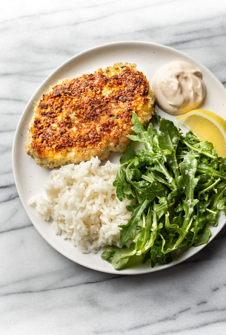 chicken patties on a plate with rice, remoulade sauce, arugula salad, and a lemon wedge