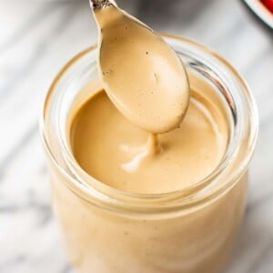 close-up of creamy balsamic dressing being drizzled from a spoon over a glass jar of dressing