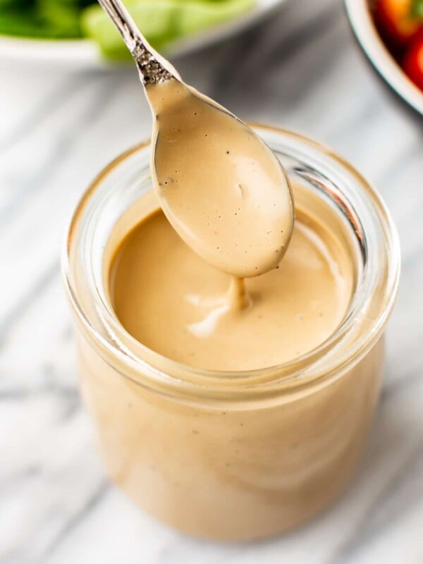 close-up of creamy balsamic dressing being drizzled from a spoon over a glass jar of dressing