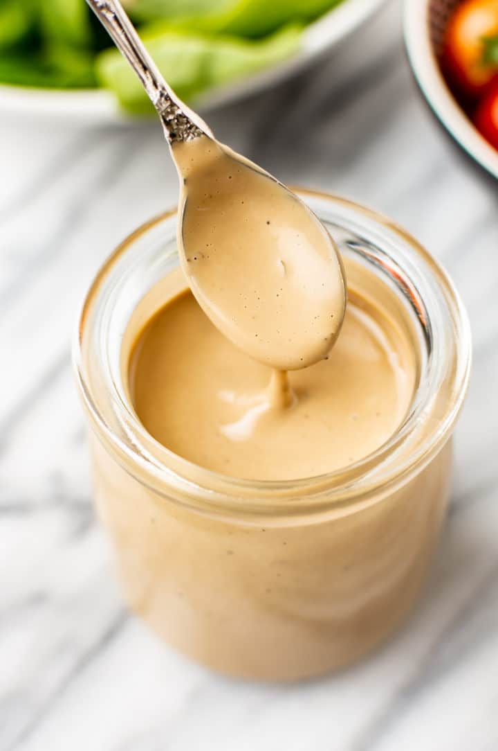 close-up of creamy balsamic dressing being drizzled from a spoon over a glass jar of dressing