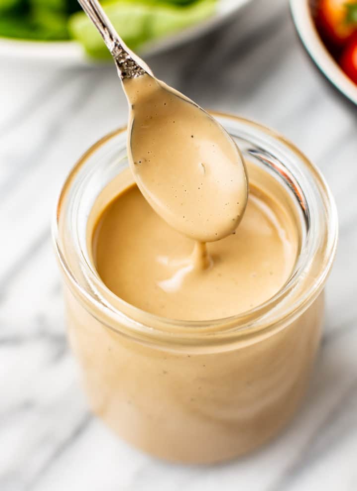 close-up of creamy balsamic dressing being drizzled from a spoon over a glass jar of dressing