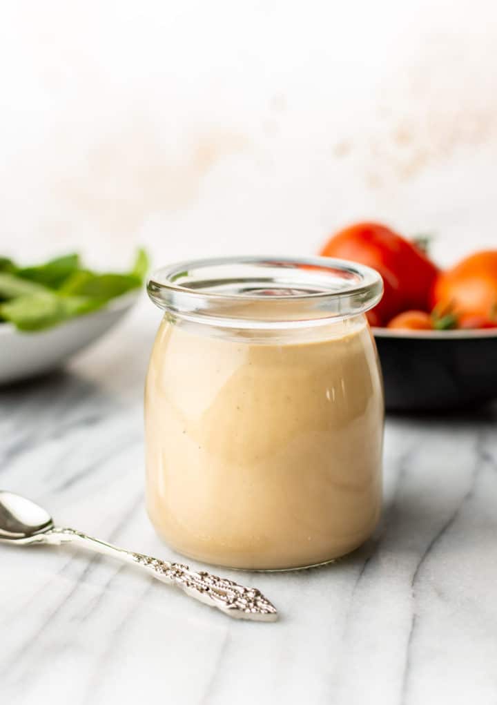 a jar of creamy balsamic dressing with a small spoon beside it and salad veggies in the background